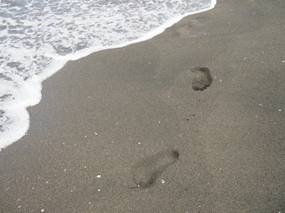 foot prints on a black sand beach with tilt-shift blur. Surf in background. Concept for loneliness, solitude, depression.