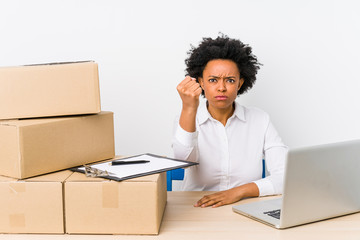 Warehouse manager sitting checking deliveries with laptop showing fist to camera, aggressive facial...