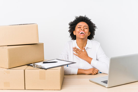 Warehouse manager sitting checking deliveries with laptop laughs out loudly keeping hand on chest.