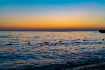 Красивый, красочный и контрастный закат над морем, океаном. Горячее солнце освещает просторный пейзаж, отбрасывая блики лучей на водную гладь. Яркий солнечный восход. Путешествие и туризм.