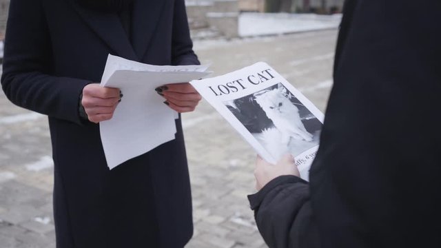 Unrecognizable Caucasian man giving missing cat ad to young woman on the street, people going out the shot in different directions. Owner searching for his pet. Loss, search.