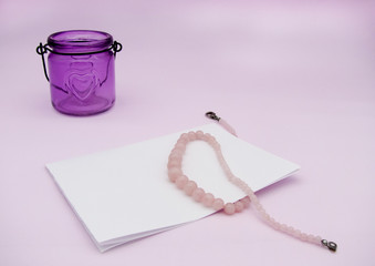 Blank sheet for writing, rose quartz beads and purple candlestick with a heart on a pink background. Letter. Mockup. An empty list 