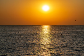 Fototapeta premium Красивый, красочный и контрастный закат над морем, океаном. Горячее солнце освещает просторный пейзаж, отбрасывая блики лучей на водную гладь. Яркий солнечный восход. Путешествие и туризм.
