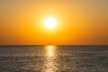 Красивый, красочный и контрастный закат над морем, океаном. Горячее солнце освещает просторный пейзаж, отбрасывая блики лучей на водную гладь. Яркий солнечный восход. Путешествие и туризм.
