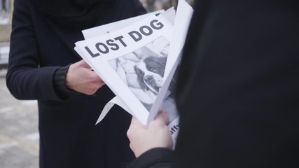 Close-up of male Caucasian hands giving missing dog ad to unrecognizable woman. People searching for their lost pet on streets. Despair, loss.