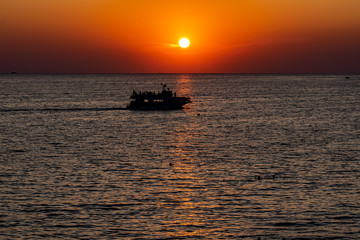 Красивый, красочный и контрастный закат над морем, океаном. Горячее солнце освещает просторный пейзаж, отбрасывая блики лучей на водную гладь. Яркий солнечный восход. Путешествие и туризм.