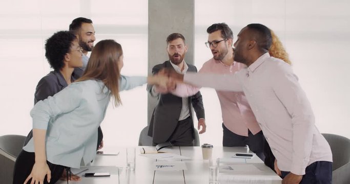 Multiethnic group of office workers putting their hands together at the end of meeting. Young employeers celebrating together with team cheer and applouds. Concept of unity and teamwork.