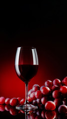 Glass of a red wine with grapes on a black mirror background with reflections