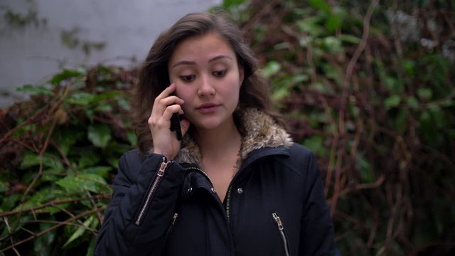 Very Upset Young Mixed Woman Talking on the Phone Outside with Winter Jacket on
