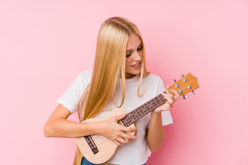 Young blonde woman playing ukelele isolated in a background