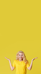 Young happy woman shows hands up, spreads his hands to the sides. Above is an empty place for text and inscription on a yellow background. vertical shot