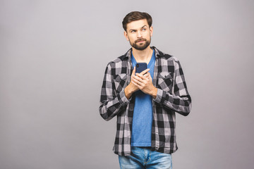 Always in touch. Serious young man holding smart phone and looking at it. Portrait of a happy young man using mobile phone isolated over grey background.