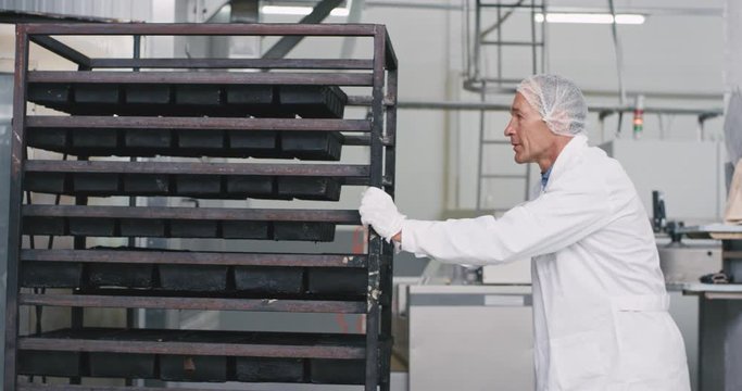Closeup old professional worker and assistant load the shelves of bread in the industrial oven machine to get baking the bread they wearing special equipment white uniform