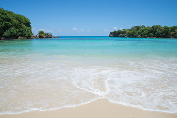 Shore of Winnifred Beach, Jamaica. Turquoise waters, little waves and ripples. Blue sky and green trees in the background
