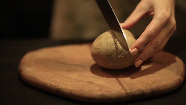a woman in the kitchen cuts a Sapodilla on a wooden Board