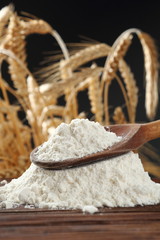 Wheat flour on wooden spoon at wheat ears background