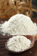 Fototapeta na wymiar Wheat flour on wooden spoon at wheat ears background