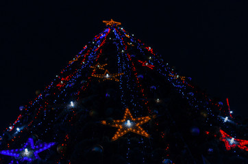 a giant glittering Christmas tree against the dark night sky. new year garlands stars sparkle. low view angle.