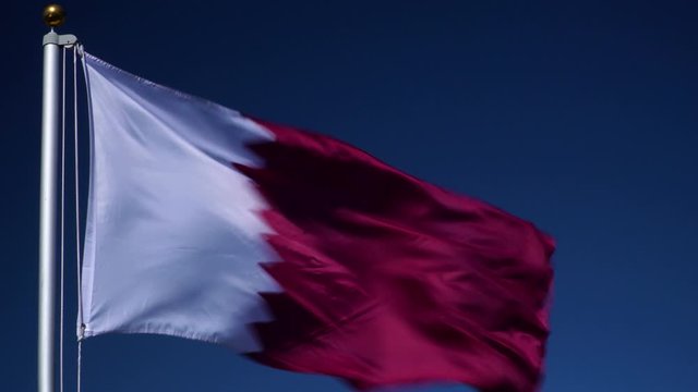 Qatar Flag flying in the wind outdoors with Blue sky behind - Qatari flag on flagpole.