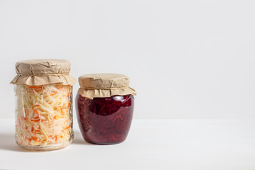 Homemade sauerkraut with carrots and cabbage salad with beets in a glass jar on a white wooden background. Fermented food.