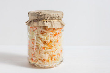 Homemade sauerkraut. Fermented food. Sauerkraut with carrots in a glass jar on a white wooden background