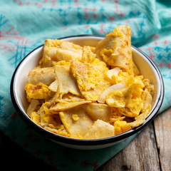 Mexican scrambled eggs with corn tortilla also called migas on wooden background