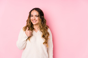 Young curvy woman posing in a pink background isolated smiling and raising thumb up