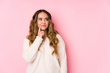 Young curvy woman posing in a pink background isolated looking sideways with doubtful and skeptical expression.