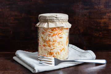 Homemade sauerkraut with carrots in a glass jar on a dark wooden background. Fermented food. Marinated vegetables