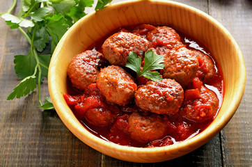 Fried meatballs in tomato sauce in wooden bowl