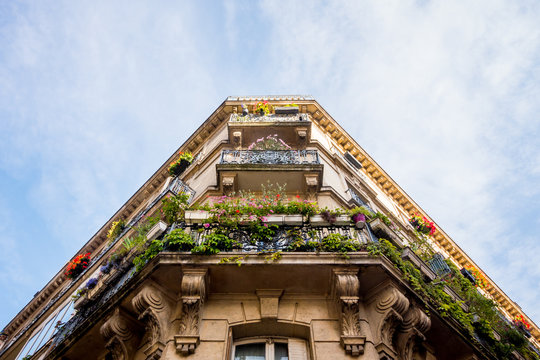 Looking up at corner apartments with balconies filled with flowers in Paris, France.