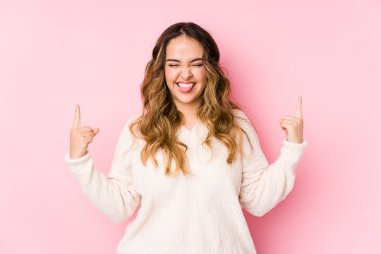 Young curvy woman posing in a pink background isolated showing rock gesture with fingers