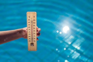 Woman holding thermometer on the pool background. Hot weather and summer concept