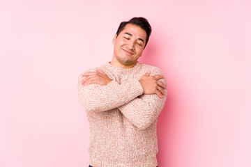 Young curvy man posing in a pink background isolated hugs, smiling carefree and happy.