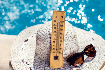 Woman's hat, thermometer and sunglasses lying beside the pool. Hot weather and summer concept