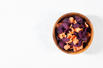 Dried carrot and beet chips in a wooden bowl and raw carrots, beets on a white concrete background. Organic natural food.