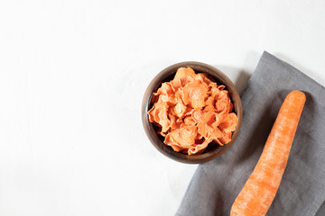 Dried carrot chips in a wooden bowl on a black stone background. Organic natural food.