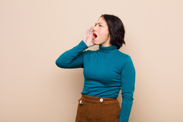 young pretty woman yelling loudly and angrily to copy space on the side, with hand next to mouth...
