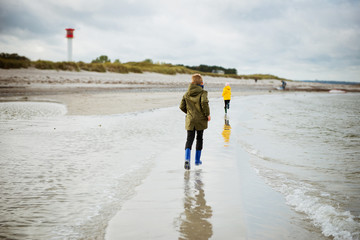 Two happy children running and jumping on water of Baltic sea in rubber boots