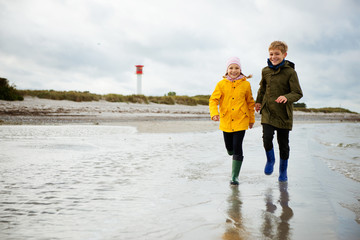 Two happy children running and jumping on water of Baltic sea in rubber boots