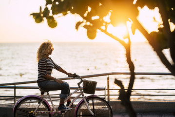 Adult beautiful caucasian woman enjoying the sunset on a vintage bike looking at the ocean - outoor people leisure activity with relax feeling and freedom - active lady and nature - Powered by Adobe