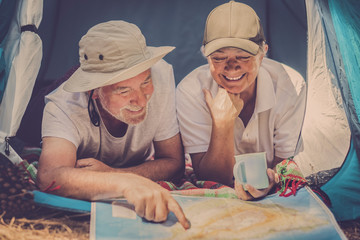 Happy senior traveler people together looking a paper map to choose the next holiday vacation travel destination - wanderlust no age limit lifestyle concept  inside  a tent in outdoor nature