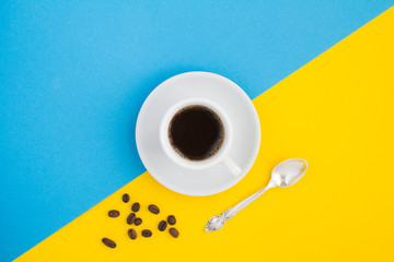 Black coffee in the white cup and coffee beans on the two-color background. Copy space. Top view.