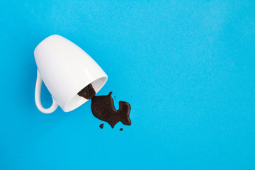 White cup with spilled black coffee on the blue background. Copy space. Top view.