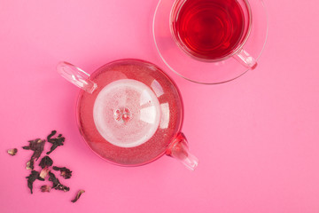 Hibiscus or karkade tea in the glass  teapot and glass cup on the pink background. Top view. Copy space.