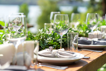Beautifully decorated wooden table in a summer open-air cafe. Green branch and fresh flowers table decoration