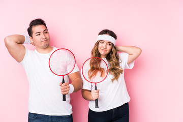 Young couple playing badminton isolated touching back of head, thinking and making a choice.