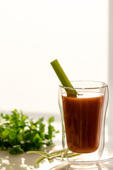 Tomato juice in a glass with celery and parsley, on a white background, close-up