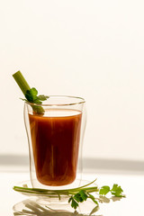 Tomato juice in a glass with celery and parsley, on a white background, close-up
