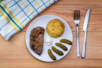 Prepared beef steak with rice risotto, pickles and sauce on white plate on wooden table background